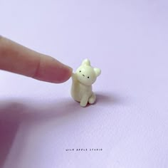 a tiny toy bear sitting on top of a white paper next to a finger pointing at it