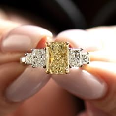 a fancy yellow diamond ring is being held in someone's hand with three diamonds around it