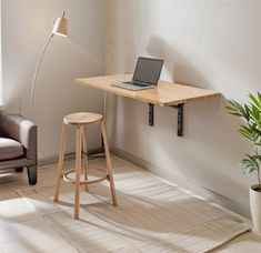 a laptop computer sitting on top of a wooden desk next to a chair and potted plant