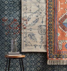 two rugs are hanging on the wall next to a small table with flowers in it