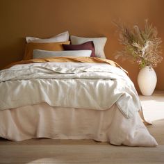 a bed with white sheets and pillows in a room next to a potted plant