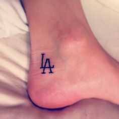 a small foot tattoo with the letter la on it's left side, in black ink