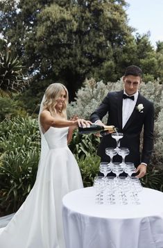 a bride and groom are cutting their wedding cake with wine glasses on the table in front of them