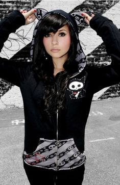 a girl with long black hair wearing a hoodie and holding her hands behind her head