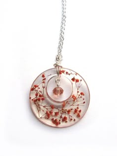 a white plate with red flowers on it is hanging from a silver chain that also has a glass bead around the edge