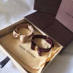 two bracelets sitting in a box on top of a white sheet covered bed with the words louis vuitton printed on it