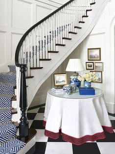 a white table topped with a lamp next to a stair case and pictures on the wall