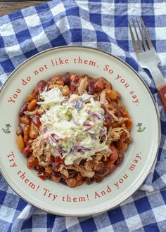 a white plate topped with beans and coleslaw next to a knife and fork