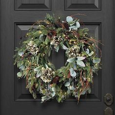 a wreath with pine cones and greenery is hanging on the front door's black door