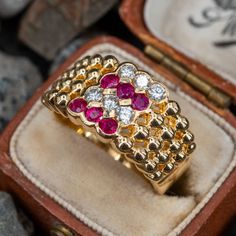 a gold ring with red and white stones on it in a box next to some rocks