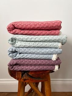 several blankets stacked on top of each other in different colors and sizes, sitting on a stool