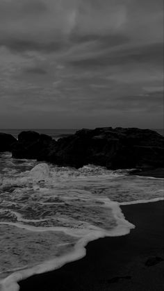 black and white photograph of waves crashing onto the beach with rocks in the foreground