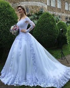 a woman wearing a blue wedding dress standing in front of bushes