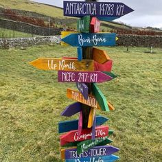 a wooden sign with many different colored signs on it's side in the grass