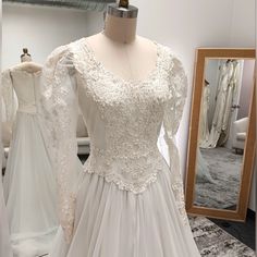 a white wedding dress on display in front of a mirror and mannequins