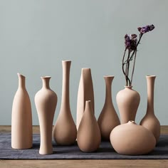 there are many vases on the table with one purple flower in it, and two white ones behind them