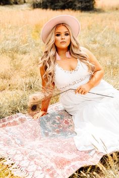 a beautiful woman sitting on top of a blanket in a field