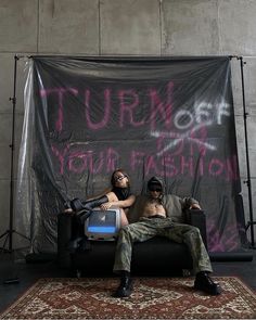 two people sitting on a couch in front of a sign that says turn off your fashion