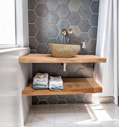 a bathroom with a sink, towel rack and tiled wall behind it in grey tones