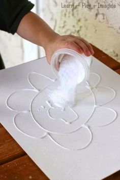 a child's hand is sprinkling cotton onto a piece of paper on a table