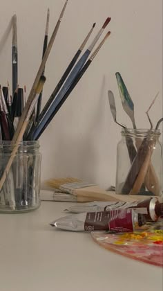 an assortment of paint brushes in a glass jar on a table next to other art supplies