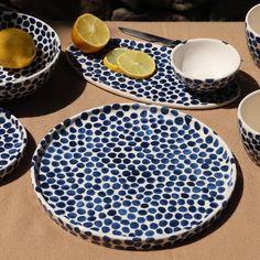 blue and white plates with lemons on them sitting on a brown table cloth next to bowls