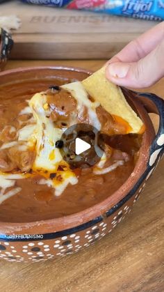 a hand holding a tortilla chip over a bowl of chili cheese and beans