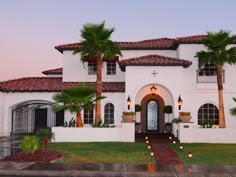 a large white house with palm trees and lights on the front door is shown at dusk