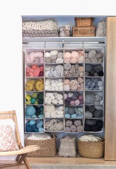 a shelf filled with lots of yarn next to a chair and basket on the floor