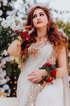 a woman in a white sari with flowers on her head and hands behind her back