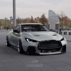 the front end of a silver sports car parked in a parking lot next to a building