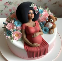 a pregnant woman sitting on top of a cake next to a teddy bear and flowers