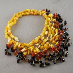 two necklaces made out of yellow and black glass beads on a gray surface with one bead in the middle