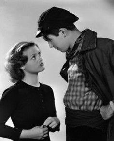 a man standing next to a woman in front of a white wall wearing a hat