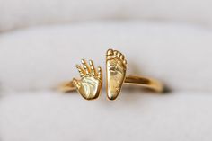 two gold rings with hands on them sitting on a white cushioned surface in front of the ring