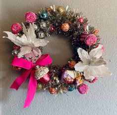 a christmas wreath hanging on the wall with ornaments around it and pink ribbon tied to it