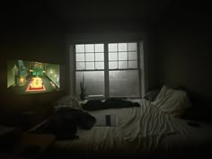 an unmade bed in front of a large window with a tv on the wall