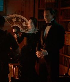 a man and woman dressed in period clothing standing next to each other near a bookshelf