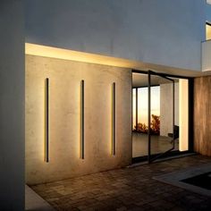 an entrance to a modern house with glass doors and lights on the outside wall at night