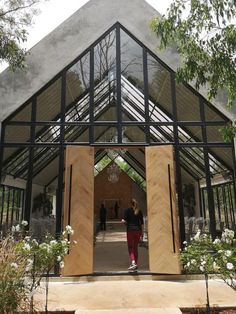 two people walking into a glass and wood structure in the middle of a garden area