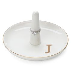 a white and gold plate with a ring holder on the bottom that has a single diamond in it