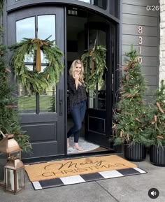 a woman standing at the entrance to a house with wreaths and christmas trees in front of her