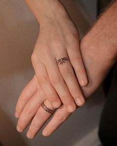 two people holding hands with tattoos on their fingers