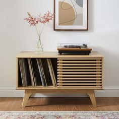 a record player sitting on top of a wooden cabinet next to a vase with flowers