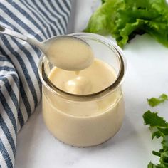 a glass jar filled with dressing next to lettuce and a spoon in it