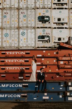 a bride and groom are sitting on the back of a train car in front of cargo containers