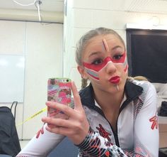 a woman with her face painted and holding up a cell phone in front of her