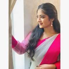 a woman in a pink and white sari standing next to a window with her hands on her hips