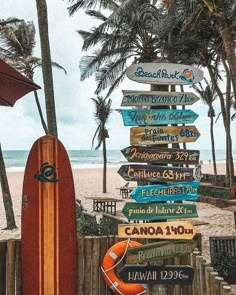 a surfboard sitting on top of a beach next to a wooden fence and palm trees