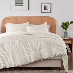 a bed with white and beige striped comforter on top of it next to a wooden headboard